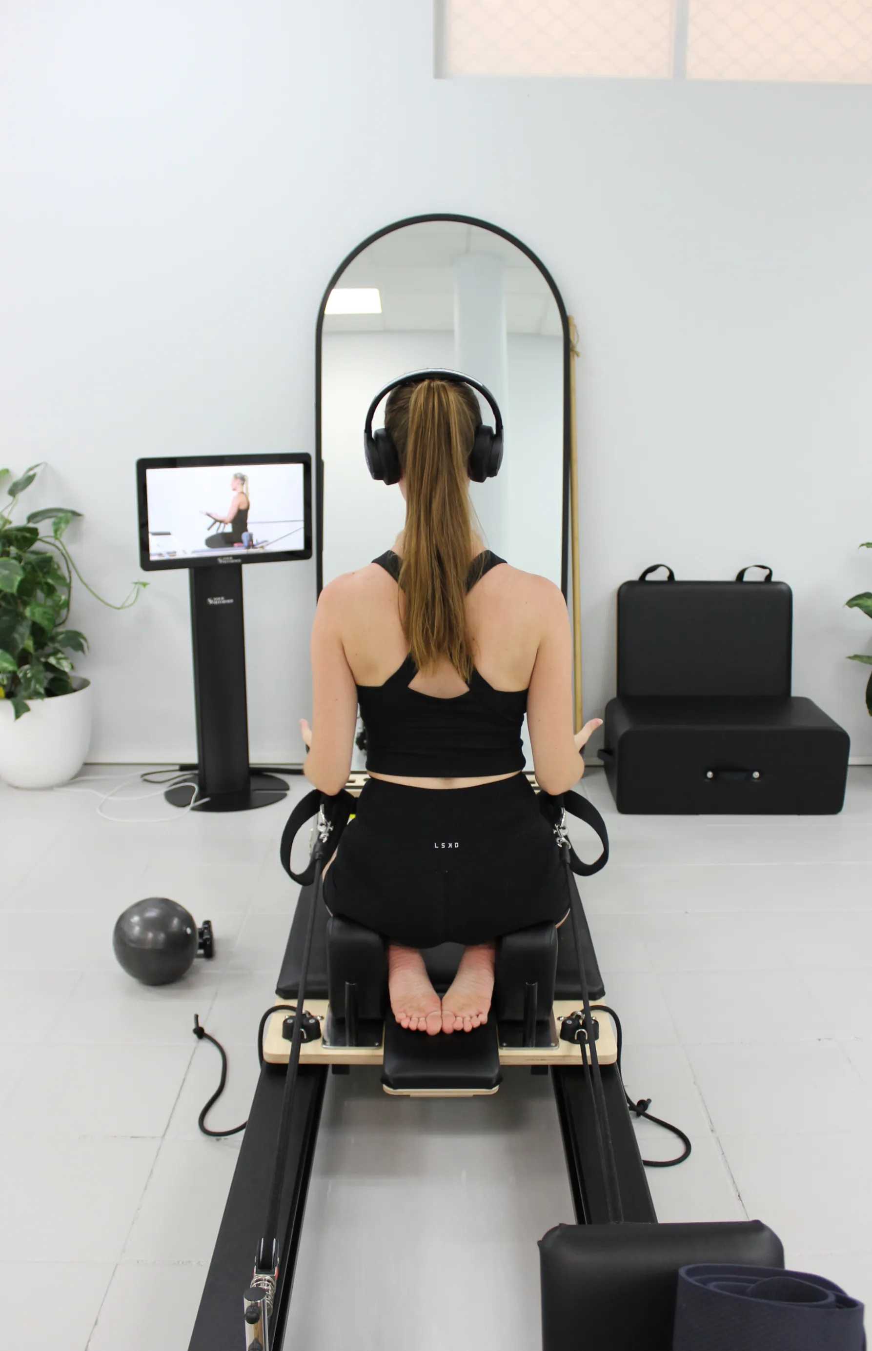 A member part-way through a class, headphones on, facing the screen at the end of the reformer