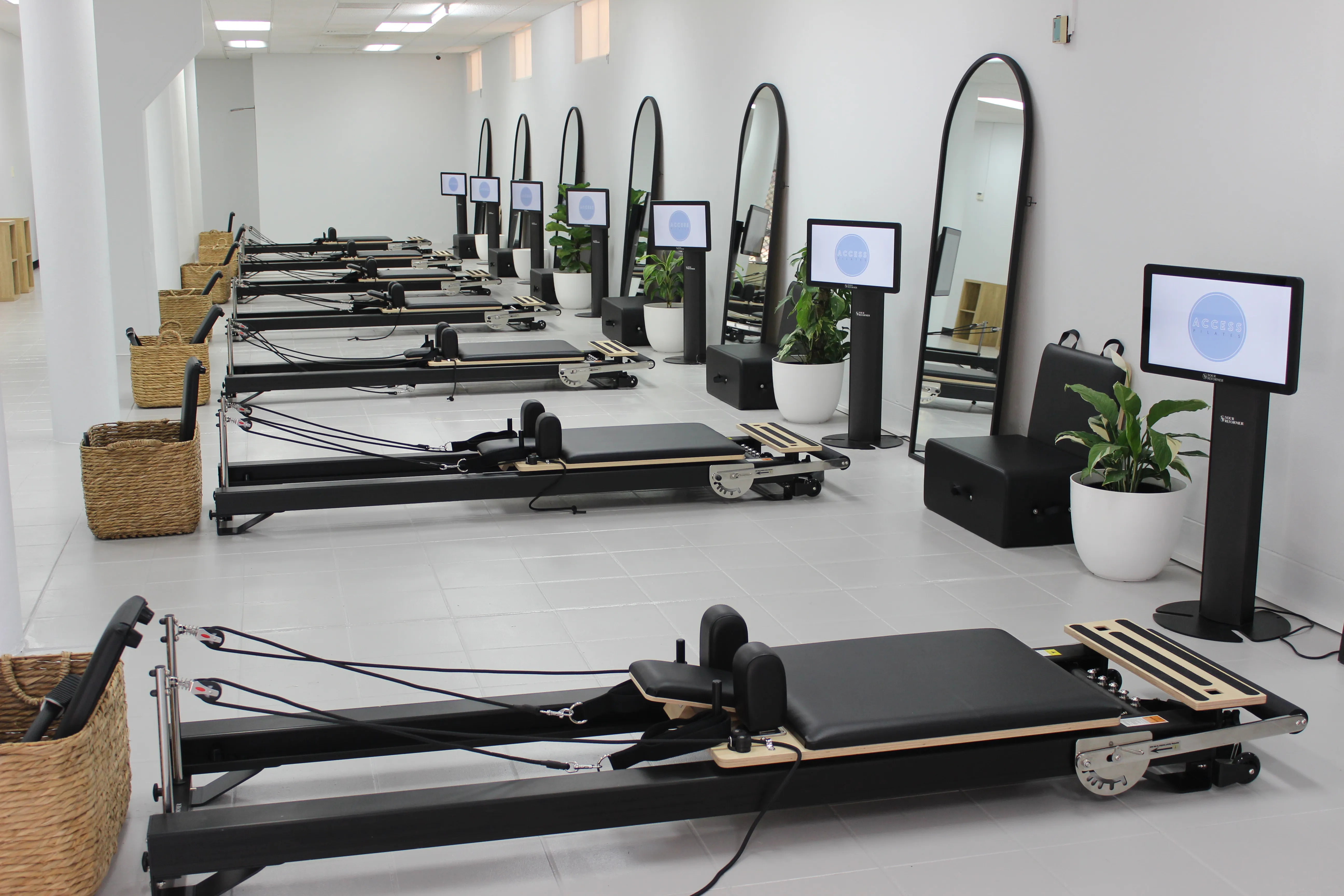 A row of reformers in an Access Pilates studio, each with its own screen and arched mirror
